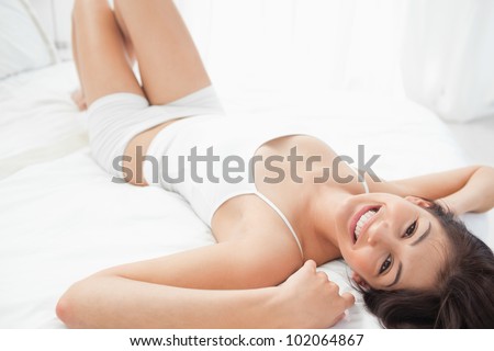 A woman lying down the length of the bed with her arms by her head, her knees raised and smiling.