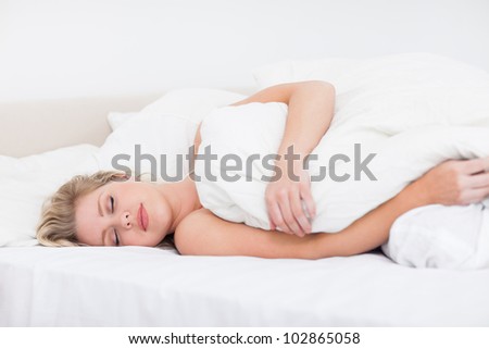 Young woman sleeping under a white duvet on her bed