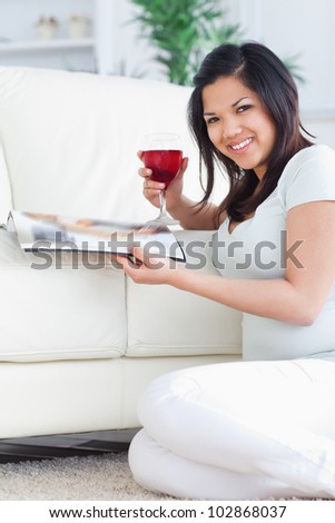 Smiling woman holding a glass of red wine and a magazine in a living room