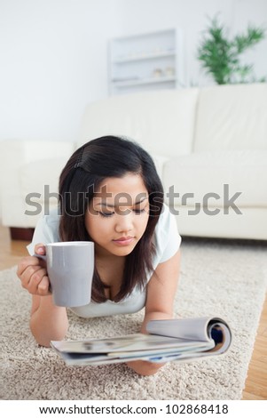 Woman holding a mug while reading a magazine on the floor in a living room