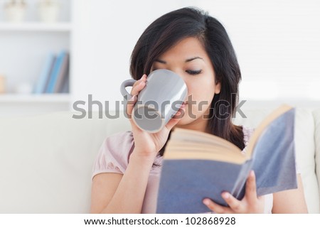 Woman drinking from a mug while holding a book in a living room