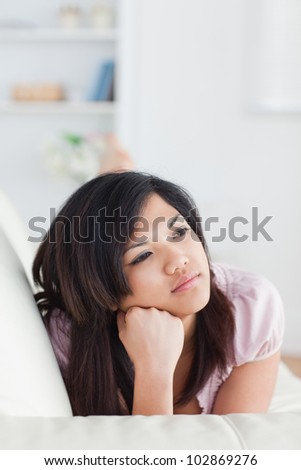 Thinking woman lying on a couch while holding her head with her fist in a living room