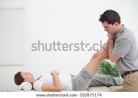 Chiropractor massaging a leg while placing it on his shoulder  in a room