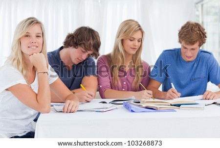 A study group working hard as one girl smiles and looks at the camera with her hand resting on her chin supporting her head