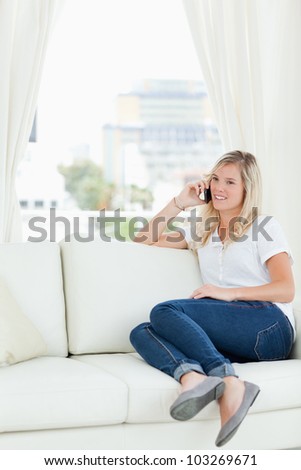 A smiling woman takes a call while sitting on the couch
