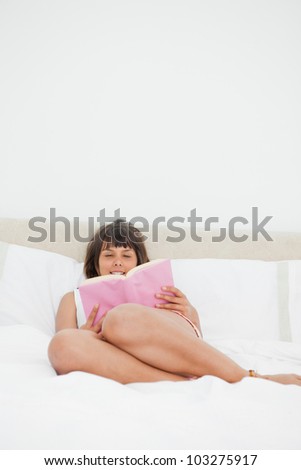 Smiling student disheveled in pajama reading a book while lying on her bed
