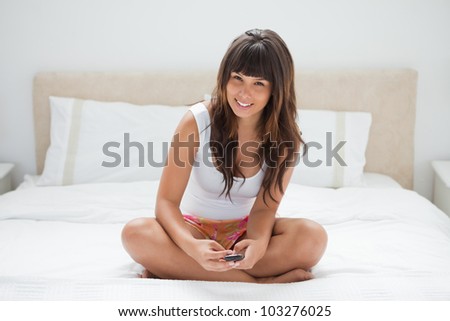 Female student crossed-legged holding a cellphone on her bed