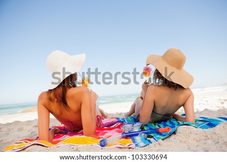Back view of beautiful women sunbathing on beach towels while sipping cocktails