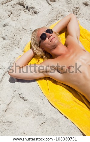 Overhead view of a blonde man lying on his beach towel while wearing sunglasses