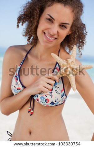 Young woman holding a beautiful starfish in front of her shoulder on the beach