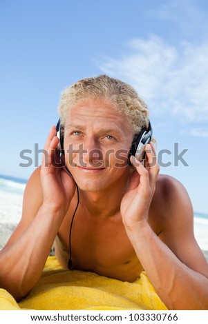 Smiling young man lying on the beach while listening to music in his headset