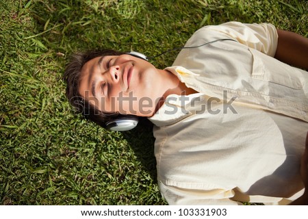Man closes his eyes as he uses headphones to listen to music while he lies down on the grass