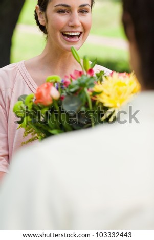 Woman laughing enthusiastically as she is given a bouquet of flowers by her friend