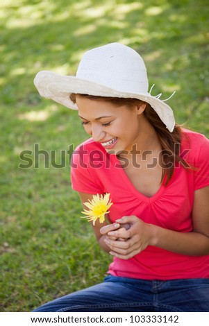 Woman laughing while wearing a white hat and holding a yellow flower as she sits on the grass