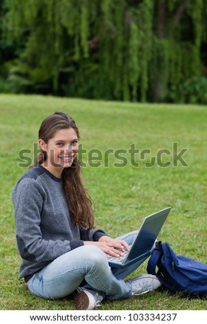 Student sitting cross-legged on the grass in the countryside while using her laptop