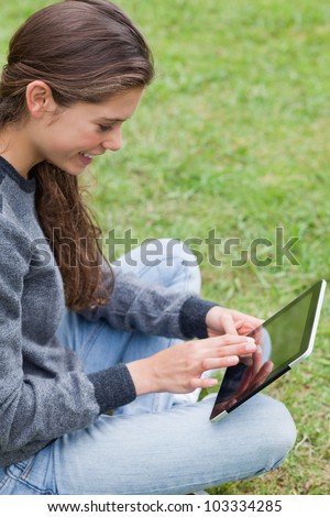 Young calm adult sitting cross-legged on the grass in a park while using her tablet pc