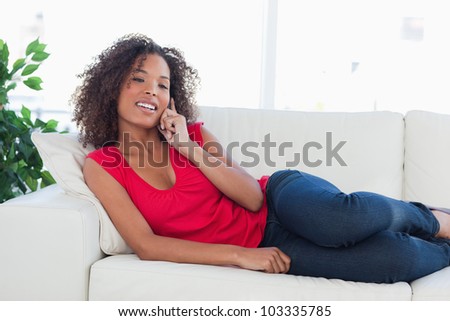 A woman lying on the couch, smiling while looking ahead and making a phone call.