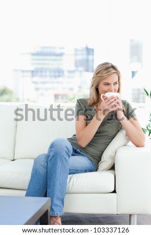A woman sitting on the couch, with a mug up to her nose, and looking to the side.