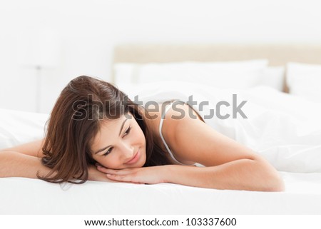 A woman lying at the end of the bed, with her head upon her hands and is looking to the side.
