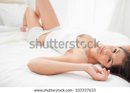 A woman with her legs slightly raised, her arms beside her head, as she rests on her back.
