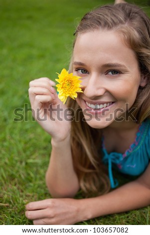 Smiling young girl showing a beautiful yellow flower while lying on the grass in a park