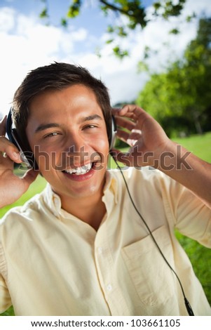 Man with a joyful expression while using headphones to listen to music in a park