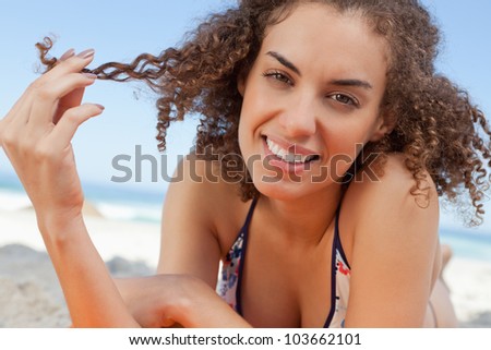 Young woman holding a lock of hair with her fingers while lying down and smiling