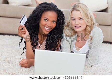 Two women are lying on the floor and looking at the camera with a laptop in front of them