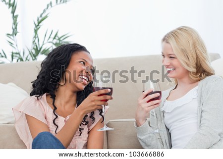 Two women are talking and drinking wine while sitting on the floor