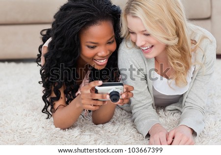 Two young women are lying on the floor at looking at photos on a digital camera