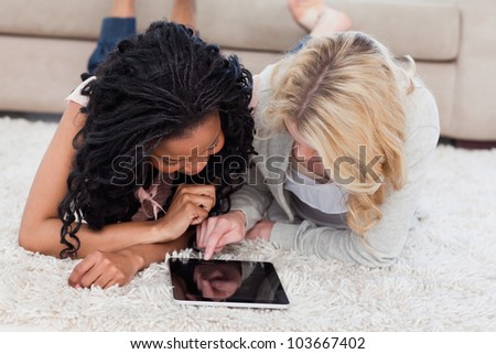 A woman is lying on the floor using a tablet computer and her friend lies next to her