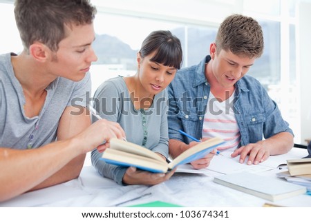 A smiling group of students working together as one uses a book to help