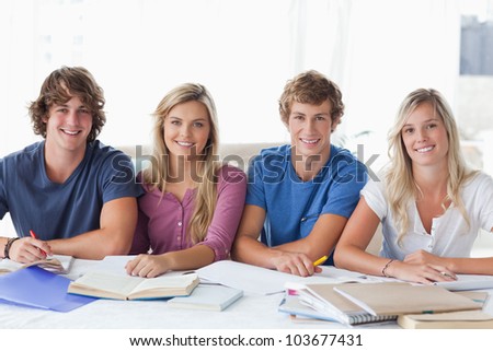 A smiling group of students doing work together as they look at the camera