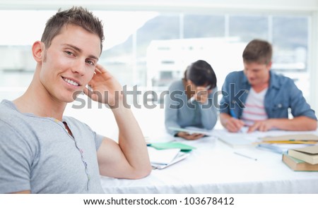 A smirking student sits in front of his friends hand on his head while his friends sit behind him working