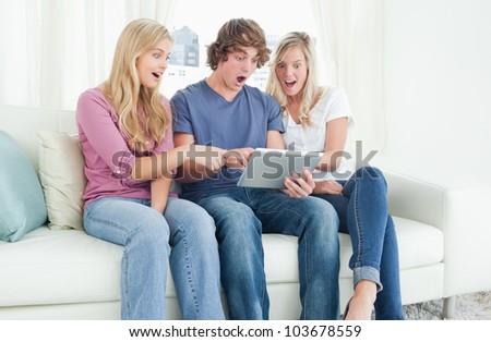 Three friends looking at the screen of the tablet and looking shocked while they point to what\'s on the screen