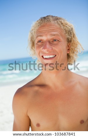 Surprised young blonde man looking towards the side while standing on the beach