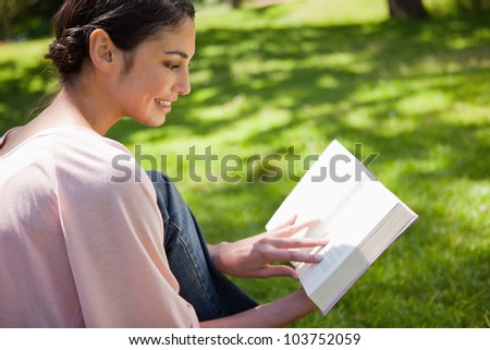Woman smiling while reading a book as she sits sits in the grass