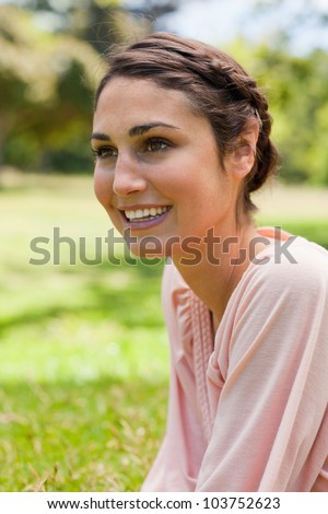 Young woman smiling while looking straight ahead of her while sitting on the grass