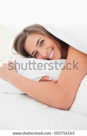 A smiling woman awake in bed looking forward with her head on the pillow.