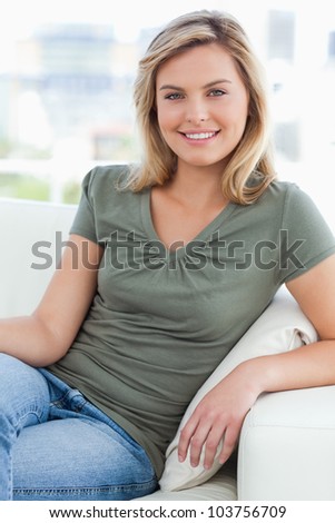 A woman looking forward with her arm on the couch arm and smiling.