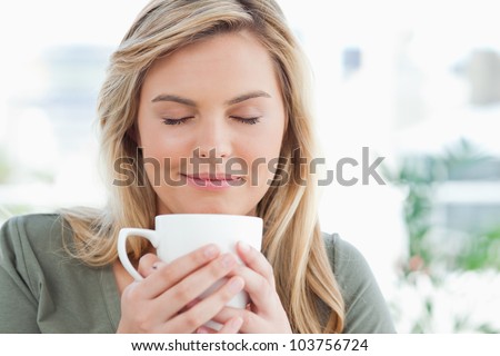 A woman with a soft smile and closed eyes, smelling the aroma from her cup in front of her.