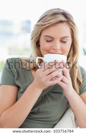 A woman holding a cup up to her nose, taking in a smell of the cups contents in front of her.