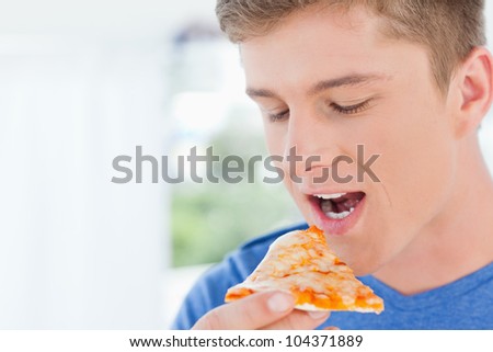 A man holding a piece of pizza near his mouth which is open as he is about to eat