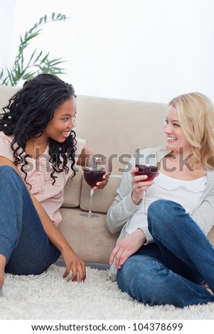 Two women are sitting on the ground and leaning against a couch