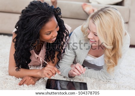 Two women lying down on the floor are looking at each other with a tablet in front of them