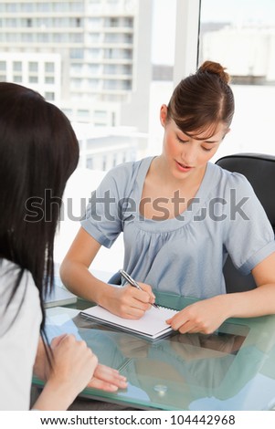 An attractive employee writes down on her pad as they other worker talks to her