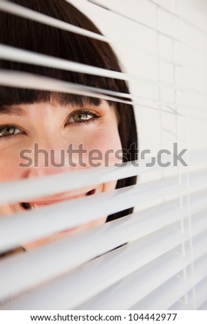 A slightly opened set of blinds with a woman looking through them