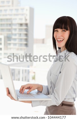 A business woman with a laptop in her hands laughs while at work