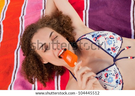 Young beautiful woman looking relaxed while eating a delicious orange ice lolly