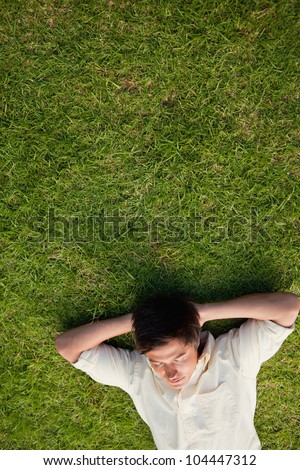 Elevated view of a man lying in grass with his eyes closed and his hands resting underneath his head